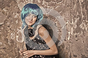 Girl in blue wig smiling with headphones on cement wall