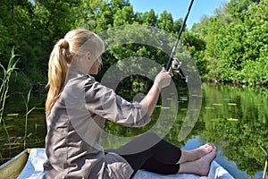 Girl in a boat is fishing in the lake