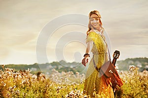 Girl in bohemian style, holding a guitar on the field with a warm and comfortable atmosphere sunset