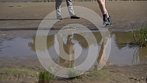 Girl in boots runs in a puddle, splashing water. Young woman on the beach.