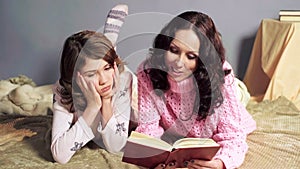 Girl bored with storybook her mother reading before bedtime, togetherness