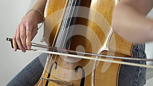 Girl bows the cello strings to play a lyrical composition. Close up.