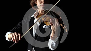 Girl bows a violin in a dark room. Black background. Close up