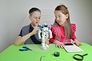 Girl and boy assemble large white object on workbench, programming its functions