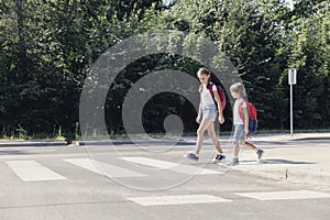Girl and boy with backpacks walking on pedestrian crossing