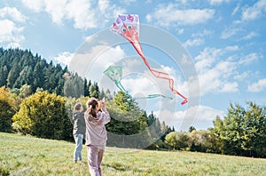 Girl and boy brother with flying colorful kites on the high green grass meadow in the mountain fields. Happy childhood moments or