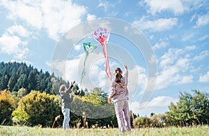 Girl and boy brother with flying colorful kites on the high green grass meadow in the mountain fields. Happy childhood moments or