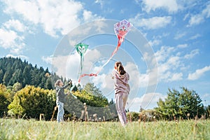 Girl and boy brother with flying colorful kites on the high green grass meadow in the mountain fields. Happy childhood moments or