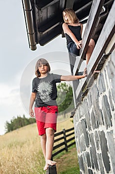 Girl and boy climbing over a wooden fence around house