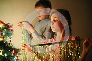 Girl and boy decorated Christmas tree with tinsel at evening