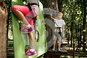 Girl and boy in equipment climbs in rope park