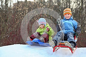Girl and boy intend drive from hill on sledges