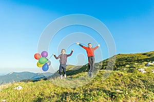 Girl and a boy jumping with outstretched arms with balloons on the mountainside