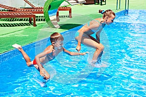 Girl and boy jumping into resort pool