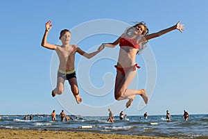 Girl and boy are jumping on  sandy sea beach. friends in  jump on sea in summer