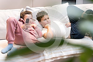 Girl and boy laying on the sofa and watching TV after school