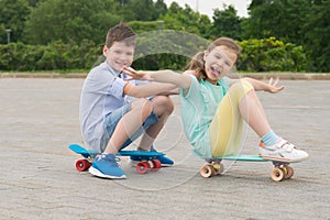 Girl and boy in the Park outdoors, riding sitting on sports boards, building funny grimaces