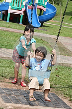 Girl & boy at the park swinging on sunny day