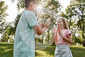 Girl and boy play patty cake game on lawn in park