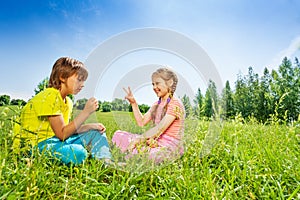 Girl and boy play rock-paper-scissors on grass