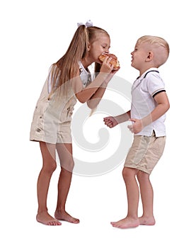 Girl and boy sharing a cinnamon bun isolated on a white background. Children eating a bun. Pastry production concept.