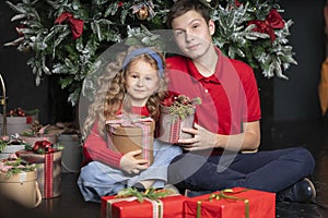 Girl and boy, sister and brother in red clothes with gifts near Christmas tree. Smiling children waiting santa for new year. Happy