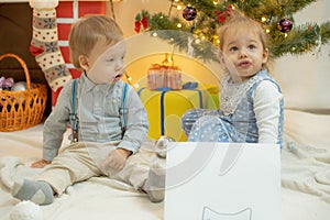 Girl and boy sit against a christmas tree and fireplace near a white sheet of paper