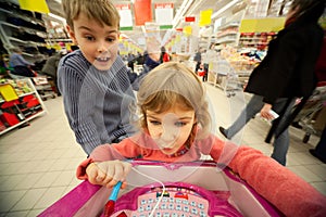 Girl and boy sit in shoppingcart, play new toy