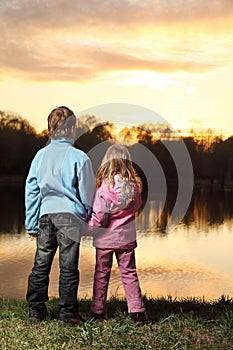 Girl and boy standing back on bank of river