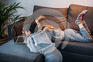 Girl and boy using laptop and lying on sofa