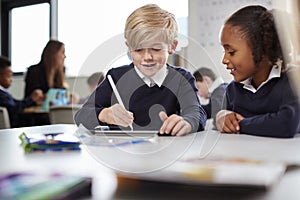 A girl and a boy using a tablet computer and stylus in a primary school class, front view, selective focus photo