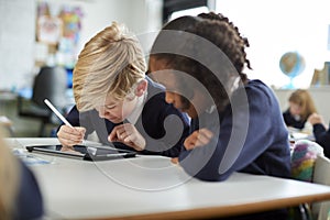 A girl and a boy using a tablet computer and stylus in a primary school class looking closely at the screen