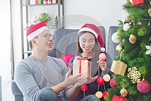 Girl with boyfriend wearing Santa hats decorating Christmas tree at home for holidays