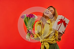 Girl brags showing tongue in a yellow blouse with a bouquet of tulips and a white box tied with red ribbon