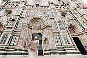 The girl-bride is with beautiful flower pattern as a mask in Florence, stylish bride in a wedding dress standing with a mask in