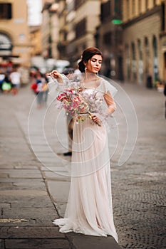 The girl-bride is with beautiful flower pattern as a mask in Florence, stylish bride in a wedding dress standing with a mask in