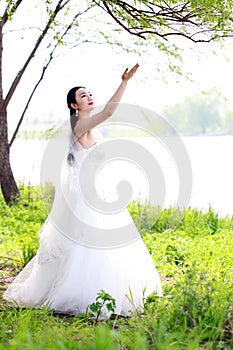 Girl bride in wedding dress with elegant hairstyle, with white wedding dress Standingin the grass by the river