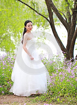 Girl bride in wedding dress with elegant hairstyle, with white wedding dress Standingin the grass by the river