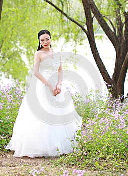 Girl bride in wedding dress with elegant hairstyle, with white wedding dress Standingin the grass by the river