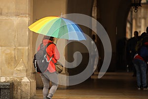 A girl in bright autumn clothes with a large umbrella of all colors of the rainbow walks in the city in the rain. Gay parade of
