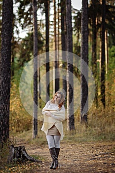 Girl in bright clothes against a background of tree trunks in the autumn forest