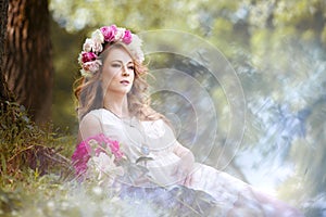 Girl in a bright dress and a wreath of peons resting on the meadow