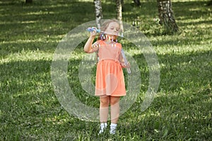 A girl in a bright orange dress blows soap bubbles in nature.