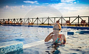 A girl in a bright swimsuit and swimming goggles poses near the pool sunbathing under the summer sun