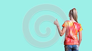 A girl in a bright tie dye t-shirt on a light turquoise background.