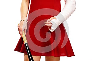 Girl with a broken arm in plaster, dressed for a party, wearing red dress, holding baseball bat