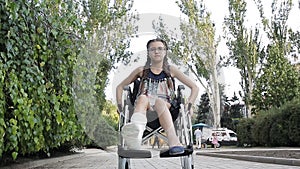A girl with a broken leg sits in a wheelchair in front of the playground.