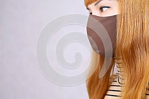 A girl in a brown cloth medical mask. a young woman with red hair in a striped turtleneck looks sideways in a protective mask