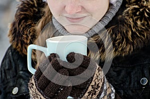 Girl in the brown gloves holding a blue mug of tea, part of the face, close-up