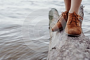 A girl in brown leather boots is standing on a log on the seashore, waves with white foam are rolling on the shore against the